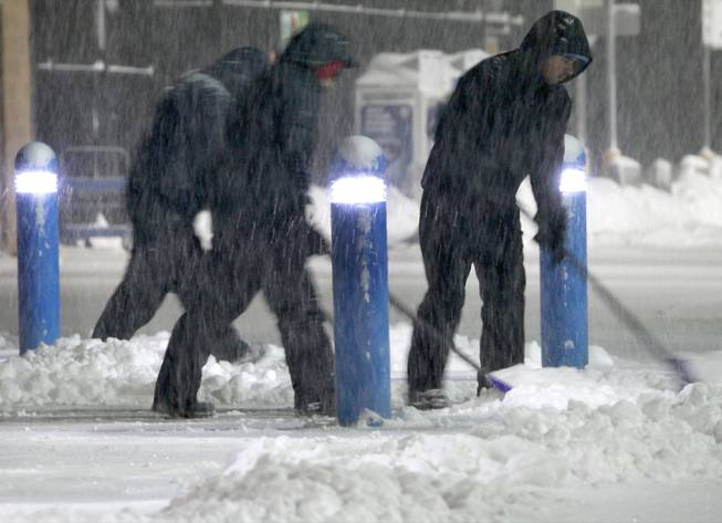Workers clears snow from the sidewalk outside a business Saturday, Feb. 15, 2014, in the Boston suburb of Hudson, Mass. Another round of snow made its way into the Northeast on the heels of a storm that brought snow and ice to the East Coast, caused at least 25 deaths and left hundreds of thousands without power.