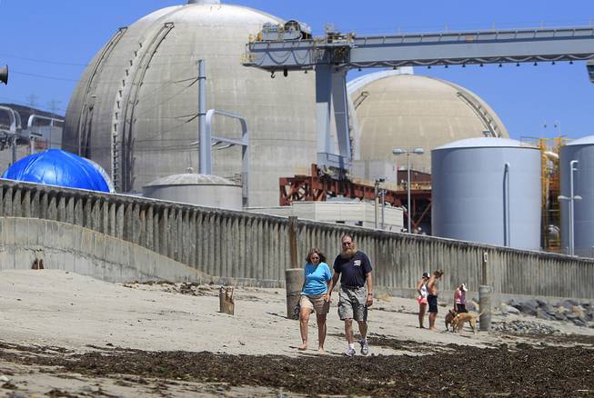 Beach-goers walk on the sand near the San Onofre nuclear power plant in San Clemente, Calif., June 30, 2011. The facility has been closed since 2012.