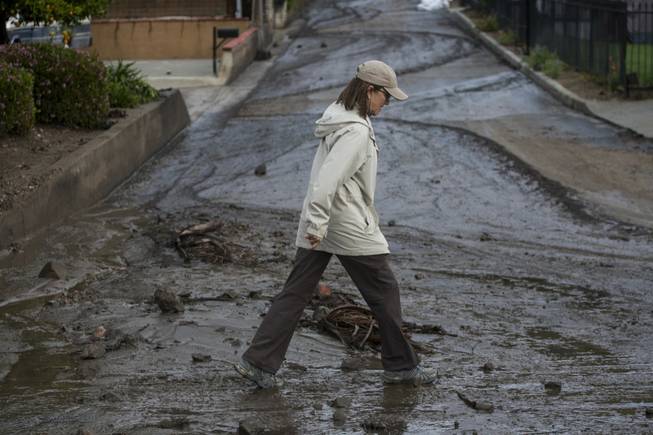 A woman walks over the mud and debris at the corner of Sierra Madre Avenue and Highcrest Road along the hillside in Glendora, Calif. on Saturday, March 1, 2014. A burst of heavy showers before dawn Saturday impacted wildfire-scarred mountainsides above foothill suburbs east of Los Angeles, causing another round of mud and debris flows in the city of Glendora.