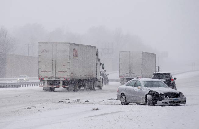 A car involved in a crash while traveling on Maryland Route 50 is passed by trucks during a snow storm, Monday, March 3, 2014, in Bowie, Md. 