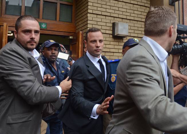 Oscar Pistorius, center, is escorted out of the high court after the first day of his trial in Pretoria, South Africa, Monday, March 3, 2014. Pistorius is charged with murder with premeditation in the shooting death of girlfriend Reeva Steenkamp in the pre-dawn hours of Valentine's Day 2013.