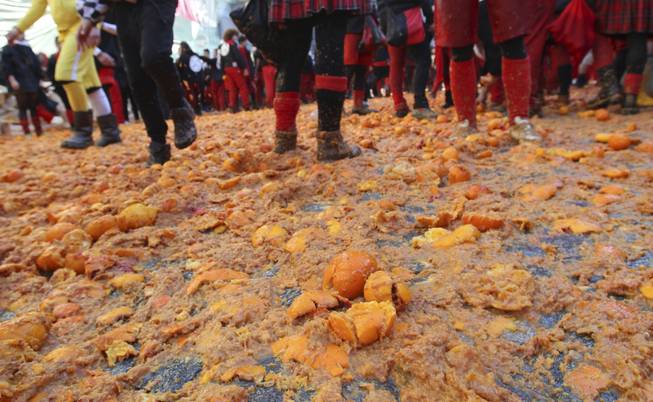 People walk over smashed oranges covering the ground during an oranges battle part of Carnival celebrations in the northern Italian Piedmont town of Ivrea, Tuesday, March 4, 2014. The traditional orange throwing battle has its roots in the middle of the XIXth century.