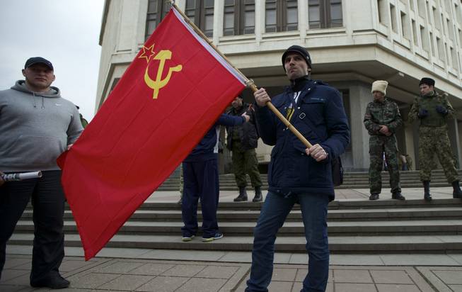 Local residents hold a Soviet flag as members of Cossack militia guard the local parliament building in Simferopol, Ukraine, on Thursday, March 6, 2014. Lawmakers in Crimea declared their intention Thursday to split from Ukraine and join Russia instead, and scheduled a referendum in 10 days for voters to decide the fate of the disputed peninsula. Russia's parliament, clearly savoring the action, introduced a bill intended to make this happen.