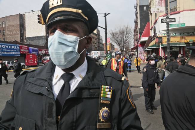 A police officers wear safety mask a block away from the site of an explosion that leveled two apartment buildings in the East Harlem neighborhood of New York, Wednesday, March 12, 2014. Con Edison spokesman Bob McGee says a resident from a building adjacent to the two that collapsed reported that he smelled gas inside his apartment, but thought the odor could be coming from outside.