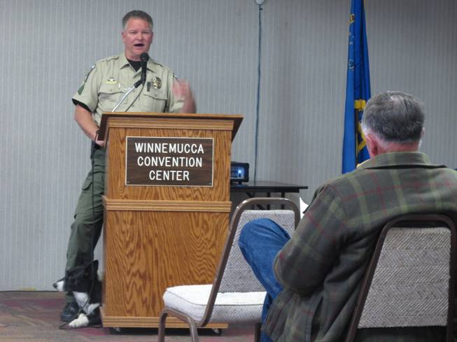 Humboldt County Sherriff's Sgt. Chris Aker describes the county's drug interdiction program on U.S. Interstate 80 in Winnemucca, Nev., Tuesday, March 11, 2014, as his K-9 "Boots'" peers out from behind the podium during a public meeting at the Winnemucca Convention Center. About 40 people attended as Sheriff Ed Kilgore and others helped respond to questions about two federal lawsuits recently filed accusing county deputies of seizing tens of thousands of dollars without bringing criminal charges against suspected drug traffickers.