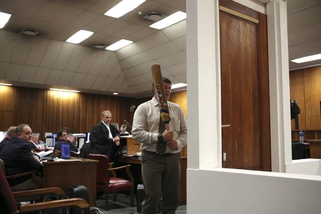 Forensic investigator Johannes Vermeulen, with a cricket bat in hand, demonstrates on a mock-up toilet and door details of how the door could have been broken down, during the trial of Oscar Pistorius in court during the second week of his trial in Pretoria, South Africa, Wednesday, March 12, 2014. Pistorius is charged with the shooting death of his girlfriend Reeva Steenkamp on Valentine's Day in 2013. At center back is prosecutor Gerrie Nel.