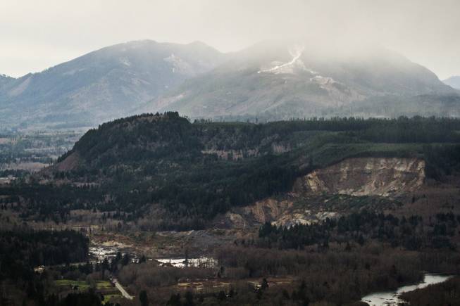 A wide aerial view shows the extensive damage of the landslide after taking out a chunk of earth from the side of the hill facing the Stillaguamish River, and down into the State Route 530, on the left, between the cities of Arlington and Darrington, on Saturday, March 22, 2014. 