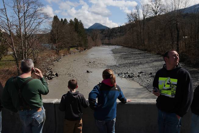 Residents watch as debris comes down the Stillaguamish River from the Whitman Road bridge east of Oso Sunday, March 23, 2014. 