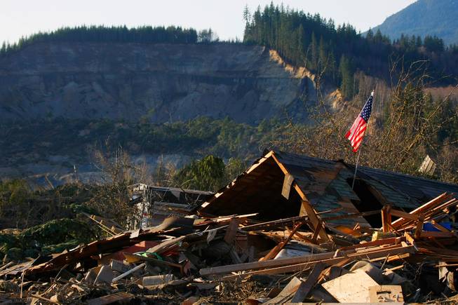 A flag sits atop what was Cory Kuntz and family's home Sunday,  March 23, 2014. The family was at a baseball game Saturday morning when the fatal mudslide swept through the area, destroying everything on their property. The area where the land broke away is seen in the background. 