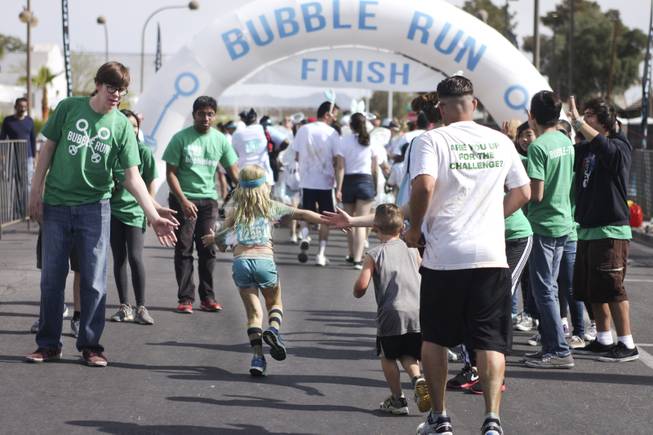Volunteers, green t-shirts, cheer on participants as they approach the finish line during the 5k Bubble Run in downtown Las Vegas Saturday, March 29, 2014.