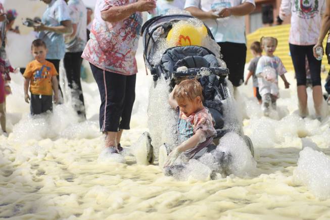 A kid slides out of a stroller after going through the yellow foam bog station during the 5k Bubble Run in downtown Las Vegas Saturday, March 29, 2014.