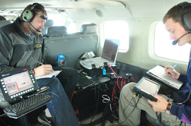 In this photo taken in October 2012, released by WSI, a Quantum Spatial Company, sensor operators Lennie Rummel left, and Drew Wendeborn, right, are shown inside a helicopter taking measurements with LIDAR, a high-tech laser system mounted on the aircraft, to build a detailed elevation map of the terrain above Omak, Wash. The maps can be used by planners and homeowners to begin to assess landslide risk.