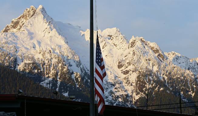 A U.S. flag hangs at half-staff with Whitehorse Mountain behind, during the early morning of Monday, March 31, 2014, at the fire station in Darrington, Wash. 