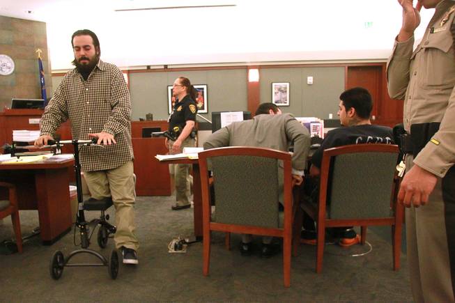 Shooting victim Christian Flores uses a rolling platform on his way out of the courtroom and past Peter Andrade Jr. during Andrade's preliminary hearing on attempted murder and other charges Tuesday, April 1, 2014.