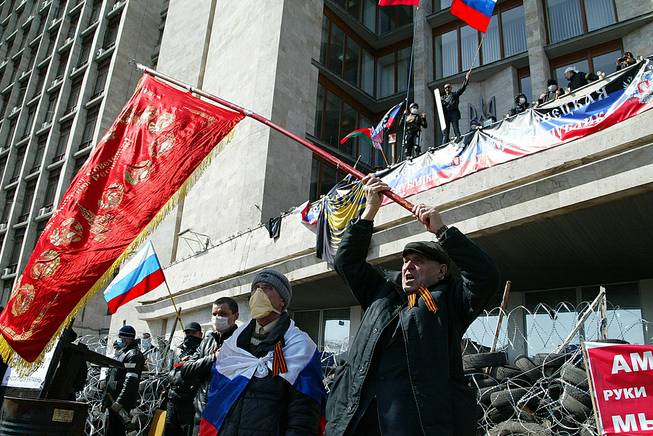Activists wave an old Soviet and Russian national flags in front of a barricade at the regional administration building, in Donetsk, Ukraine, Monday, April 7, 2014.