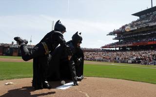 Miles Scott, dressed as Batkid, left, throws the ceremonial first pitch next to Batman before an opening day baseball game between the San Francisco Giants and the Arizona Diamondbacks in San Francisco, Tuesday, April 8, 2014. On Nov. 15, 2013, Scott, a Northern California boy with leukemia, fought villains and rescued a damsel in distress as a caped crusader through The Greater Bay Area Make-A-Wish Foundation.