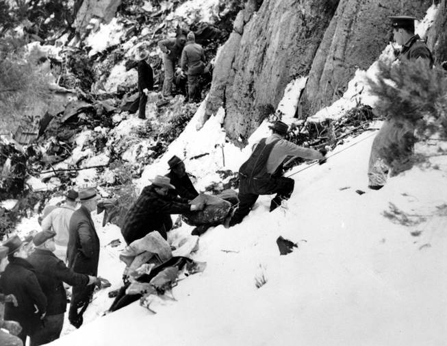 The blanket-wrapped body of film actress Carole Lombard is removed from the shattered wreckage of the Los Angeles bound TWA air liner on Table Mountain, near Las Vegas, Nev., on Jan. 18, 1942.  Lombard, 33, who was on tour to sell war bonds, and 21 other passengers, were killed when the plane crashed into the cliff high on the snow-covered mountain on Jan. 16.  In the background are searchers looking for other bodies.