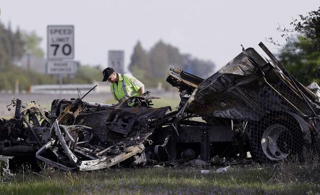 A worker looks over the demolished cab of FedEx truck that crashed into a tour bus on Interstate 5 Thursday in Orland, Calif., Friday, April 11, 2014. At least ten people were killed and dozens injured in the fiery crash between the truck and a bus carrying high school students on a visit to a Northern California College.