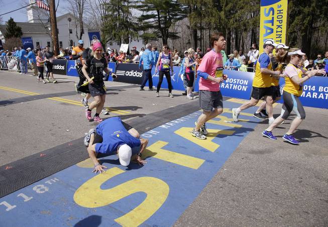 A runner toward the back of the fourth and last wave of competitors kneels to kiss the start line as he begins his running of the 118th Boston Marathon, Monday, April 21, 2014, in Hopkinton, Mass. 