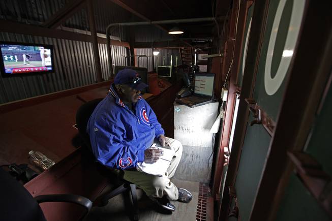 In this April 10, 2014 photo, scoreboard operator Darryl Wilson looks out to the field from inside Wrigley Field's iconic scoreboard during a baseball game between the Pittsburgh Pirates and the Chicago Cubs, in Chicago. Wilson mans the two top floors, little more than scaffolding of the three-level scoreboard, tracking scores from around baseball and changing scores and the uniform numbers of pitchers as managers in those games bring in relievers.