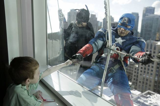 Window washers Pedro Castro, 45, as Batman, and Roberto Duran, 32, as Captain America, right, entertain patient Zakk Carrier, 5, as they hang from rope lines from the roof of the Ann & Robert H. Lurie Children's Hospital in what has become a beloved semi-annual tradition, Tuesday, April 15, 2014, in Chicago.