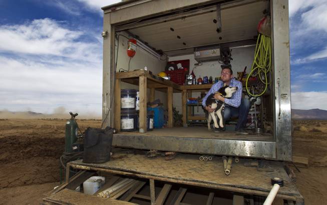 Mike Rhodes stops to play with his dog as he checks on a water-drilling rig at his father Jim's new Kingman Farms outside Kingman, Ariz., on Wednesday, April 9, 2014.