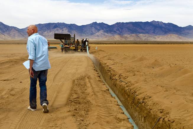 A crew works to lay more water pipe at the new Kingman Farms as Jim Rhodes trails behind outside Kingman, Ariz., on Wednesday, April 9, 2014.  The PipeMaster machine is an invention by Rhodes,which he says saves time, labor and makes the process safer.