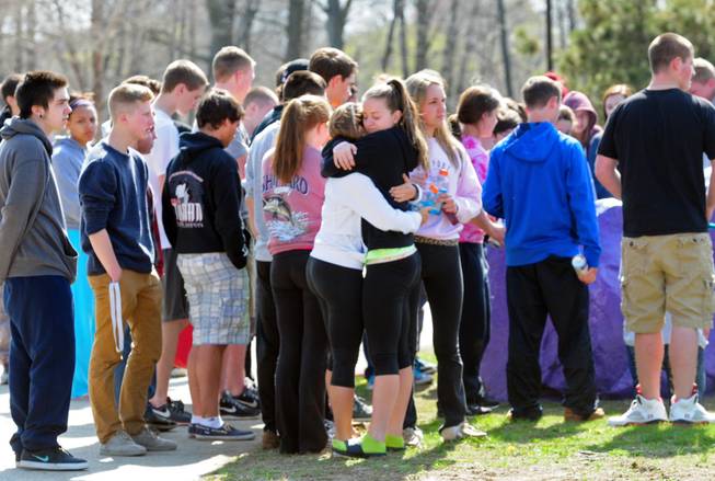 Students hug and spray paint a rock purple outside Jonathan Law High School in Milford, Conn., Friday, April 25, 2014, in memory of 16-year-old stabbing victim Maren Sanchez. Sanchez was stabbed to death earlier in the day during an altercation inside the school.