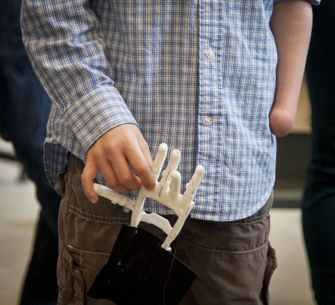 Eight-year-old Steele Songle, who was born without his left hand, holds an artificial hand designed for him by engineering students at Westtown High School, April 18, 2014, in West Chester, Pa.