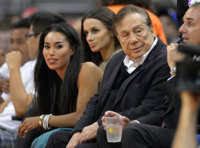 In this photo taken Friday, Oct. 25, 2013, Los Angeles Clippers owner Donald Sterling, right, and V. Stiviano, left, watch the Clippers play the Sacramento Kings. The NBA is investigating a report of an audio recording in which a man purported to be Sterling makes racist remarks while speaking to Stiviano.