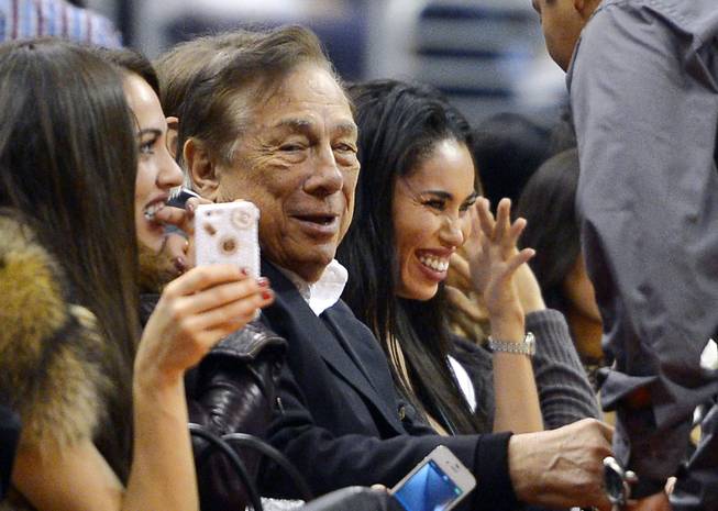 In this photo taken Oct. 25, 2013, Los Angeles Clippers owner Donald Sterling, center, and V. Stiviano, right, watch the Clippers play the Sacramento Kings during the first half of an NBA basketball game in Los Angeles. The NBA is investigating a report of an audio recording in which a man purported to be Sterling makes racist remarks while speaking to Stiviano. NBA spokesman Mike Bass said in a statement April 26 that the league is in the process of authenticating the validity of the recording posted on TMZ's website. Bass called the comments "disturbing and offensive."