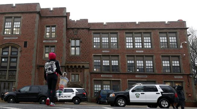 A girl crosses the street near police vehicles outside of Teaneck High School, where more than 60 students were arrested during an overnight break-in, Thursday, May 1, 2014, in Teaneck, N.J.