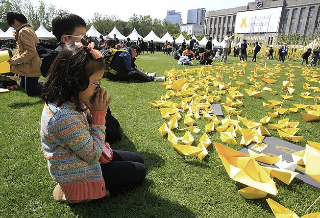 A girl prays in front of paper ships bearing messages for the victims of the sunken ferry Sewol at a group memorial altar in Seoul, South Korea, Monday, May 5, 2014. 