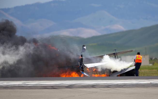 A worker fights a fire after a vintage biplane crashed upside down on a runway at an air show at Travis Air Force Base in Fairfield, Calif., Sunday, May 4, 2014. The pilot, Edward Andreini, 77, of Half Moon Bay, was killed when the plane, flying low over the tarmac, crashed and caught fire.