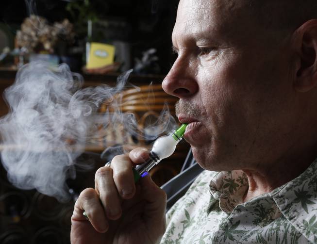 In this April 30, 2014, photo, Bill Britt, 54, who suffers from epileptic seizures and leg pain from a childhood case of polio, vaporizes medical marijuana at his home in Long Beach, Calif.