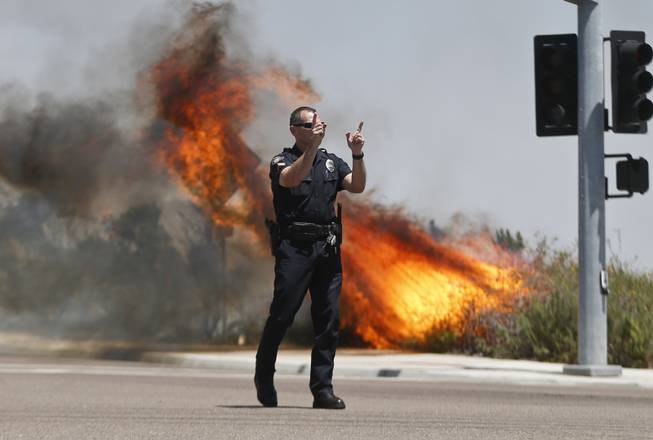 A Carlsbad,Calif. police officer turns traffic away as flames leap behind him Wednesday, May 14, 2014, in Carlsbad, Calif.  Weather conditions that at least temporarily calmed allowed firefighters to gain ground early Wednesday on a pair of wildfires that forced thousands of residents to leave their homes. 
