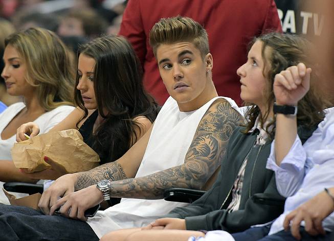 This May 11, 2014, photo shows singer Justin Bieber, center, watching the Los Angeles Clippers play the Oklahoma City Thunder with his mother, Pattie Mallette, second from left, in Los Angeles. Photographer Aja Oxman sued Bieber and his bodyguard Dwayne Patterson for assault and intentional infliction of emotion distress in Los Angeles on Wednesday, Aug. 20, over an altercation last year on Hawaii's Shipwreck Beach.