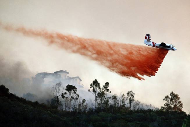 A plane drops fire retardant over a hot spot on Wednesday, May 14, 2014, in San Marcos, Calif. Wednesday, May 14, 2014, in San Marcos, Calif. Flames engulfed suburban homes and shot up along canyon ridges in one of the worst of several blazes that broke out Wednesday in Southern California during a second day of a sweltering heat wave, taxing fire crews who fear the scattered fires mark only the beginning of a long wildfire season. (AP Photo)