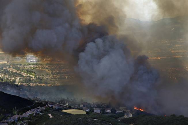 A wildfire approaches homes on Wednesday, May 14, 2014, in San Marcos, Calif. Flames engulfed suburban homes and shot up along canyon ridges in one of the worst of several blazes that broke out Wednesday in Southern California during a second day of a sweltering heat wave, taxing fire crews who fear the scattered fires mark only the beginning of a long wildfire season. (AP Photo)