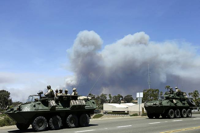 Marines move military vehicles near the entrance to Marine Corps Camp Pendleton in front of smoke plumes from the Las Pulgas wildfire burning on base Friday, May 16, 2014, in Oceanside, Calif. 