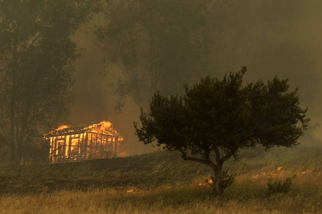 Fire engulfs a structure during a wildfire Thursday, May 15, 2014, in Escondido, Calif. One of the nine fires burning in San Diego County suddenly flared Thursday afternoon and burned close to homes, trigging thousands of new evacuation orders.