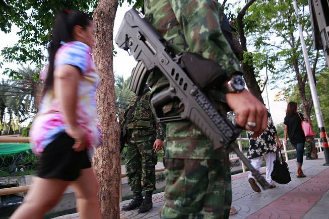 Pedestrians stroll past armed Thai soldiers guarding outside the Centre for the Administration of Peace and Order (CAPO) after soldiers were sent in to seize the center Tuesday, May 20, 2014 in Bangkok, Thailand. 