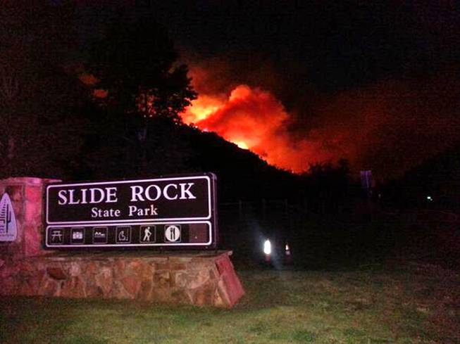 In this photo released by the Arizona Department of Public Safety, flames from a wildfire rise over a ridge behind the popular Slide Rock State Park Oak Creek Canyon near Sedona, Ariz., Tuesday, May 20, 2014. 