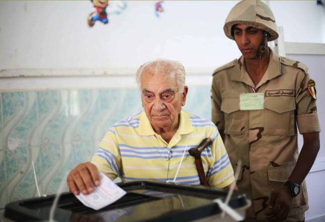An Egyptian soldier watches a voter cast his ballot in the presidential election in Cairo, Egypt, on Monday, May 26, 2014. This week’s key vote is taking place against a backdrop of the turmoil that has roiled the country since the 2011 ouster of Hosni Mubarak and the government’s crackdown against Morsi’s Muslim brotherhood and its allies since last July.