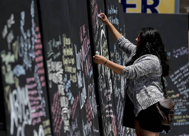 Daniela Bayon writes on a remembrance wall across the street from the IV Deli Mart, where part of the mass killings took place, on Tuesday, May 27, 2014 in the Isla Vista area near Goleta, Calif. 