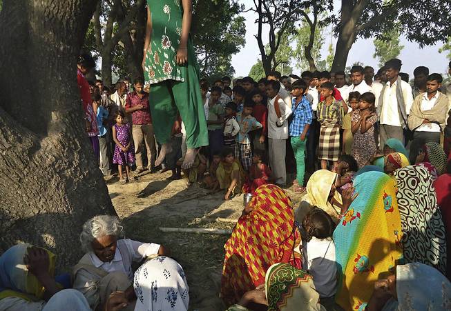 In this Wednesday, May 28, 2014, photograph, Indian villagers gather around the bodies of two teenage sisters hanging from a tree in Katra village in Uttar Pradesh state, India. 