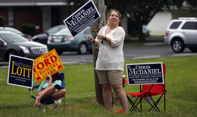 Lisa Bailey aggressively waves her campaign sign for state Sen. Chris McDaniel, who is running against incumbent U.S. Sen. Thad Cochran in the GOP primary, while Shelby Ford, 15, takes a more laid back approach to sidewalk campaigning for her father running for county chancery clerk by sitting in a lawn chair and waving his sign during the state's primary election, Tuesday, June 3, 2014, in Madison, Miss.