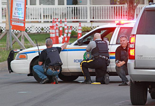 Police officers take cover behind their vehicles in Moncton, New Brunswick, on Wednesday, June 4, 2014. Three police officers were shot dead and two others injured Wednesday in the east coast Canadian province of New Brunswick.