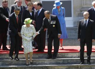 Russian President Vladimir Putin stands at right as U.S. President Barack Obama, left, and New Zealand's Governor-General Jerry Mateparae guide Britain's Queen Elizabeth II to her position for a group photo, with French President Francois Hollande, in the background, talking with German Chancellor Angela Merkel, as they take part in commemorations for  the 70th anniversary of the D-Day landings,  in Benouville in Normandy, France, Friday, June 6, 2014. 