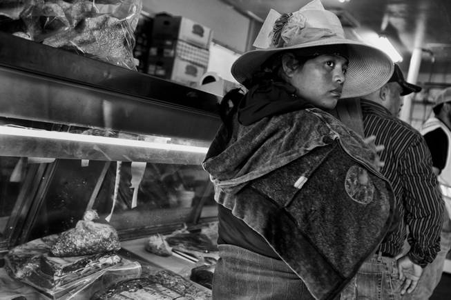 A woman just returned from working in the fields waits to make a purachase at a butcher in Huron, California. During the season the areas farms need the most labor the work force doubles, but a drought has cut production and workers find trouble landing positions in the fields.